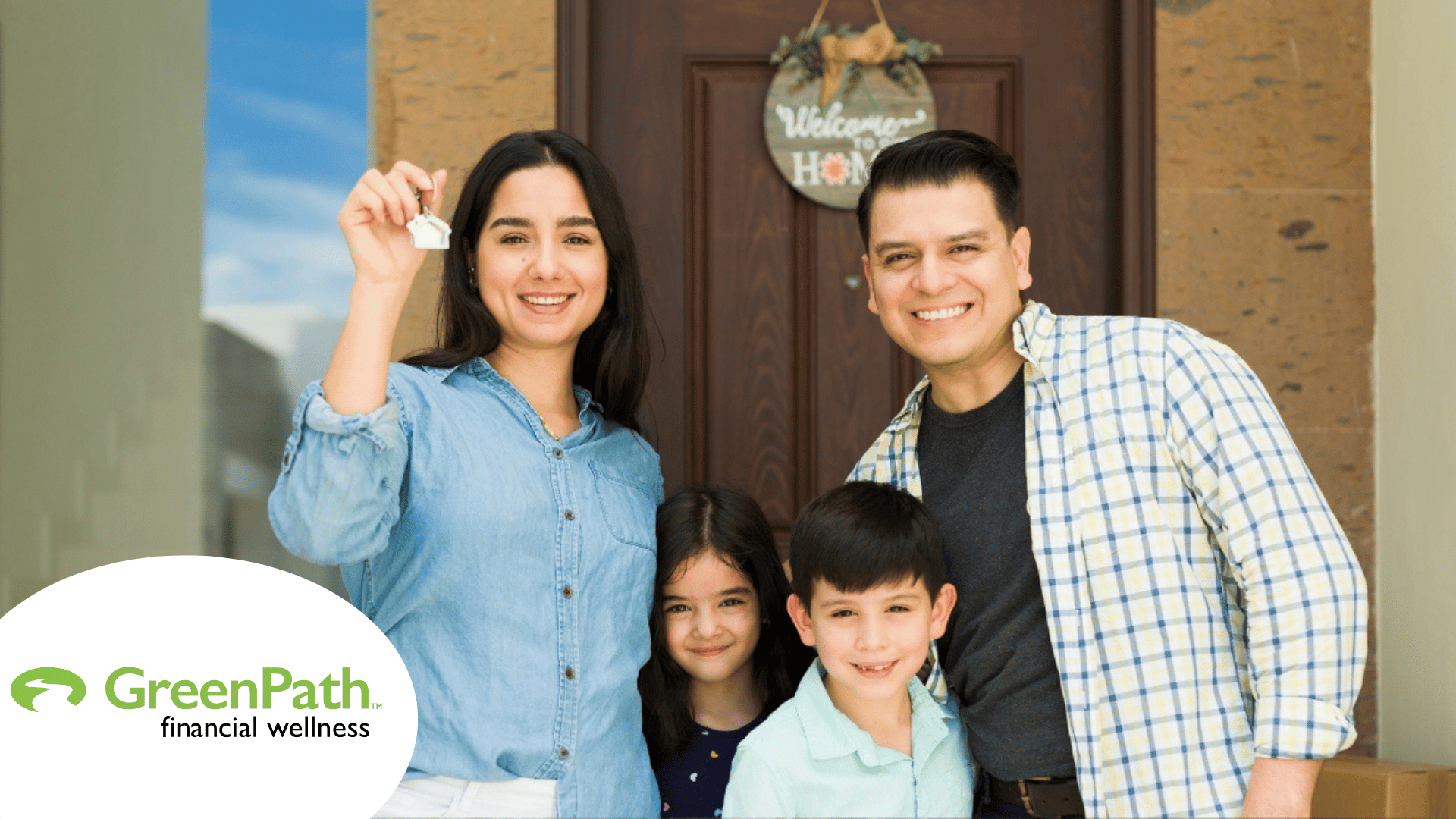 Family consisting of dad, mom, and two children standing in front of their new home. Mom is holding up a key. In the bottom left corner, the logo for GreenPath Financial Wellness appears.